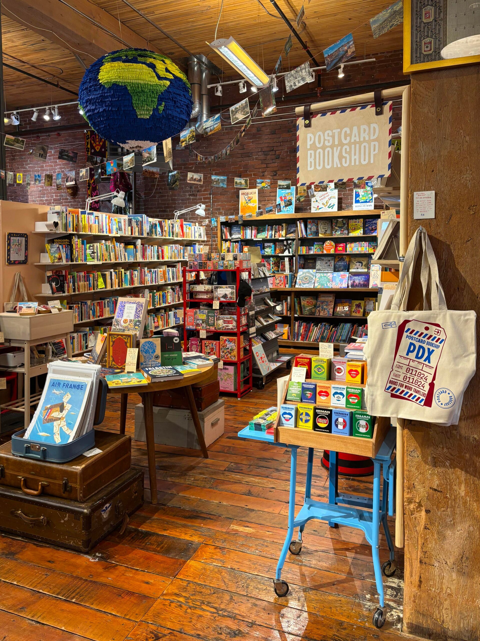 bağımsız kitapçı, Portland, Oregon, seyahat kitapları, kitap önerileri, Patrick Leonard, Postcard Bookshop, yerel işletme, kitap kulübü, CARGO Emporium, dünya edebiyatı, seyahat temalı kitaplar, Peter Hessler, Hannah Kirshner, Robert MacFarlane, ekolojik adalet, kültürel etkinlikler, yerel sanatçılar, Dia de los Muertos, kitap topluluğu, yazar tanıtımı, kitap erişimi, okuma hakkı
